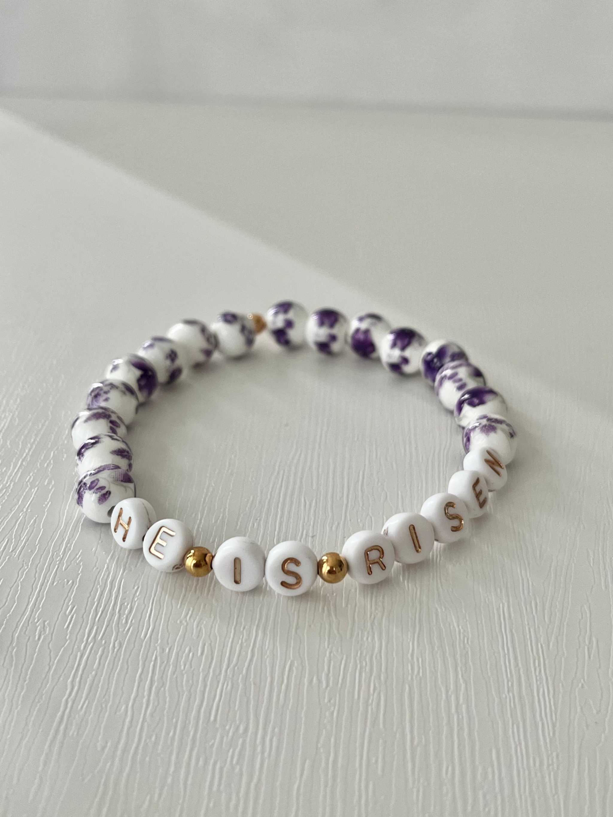 Bracelet with letter beads spelling 'HE IS RISEN' on a light background
