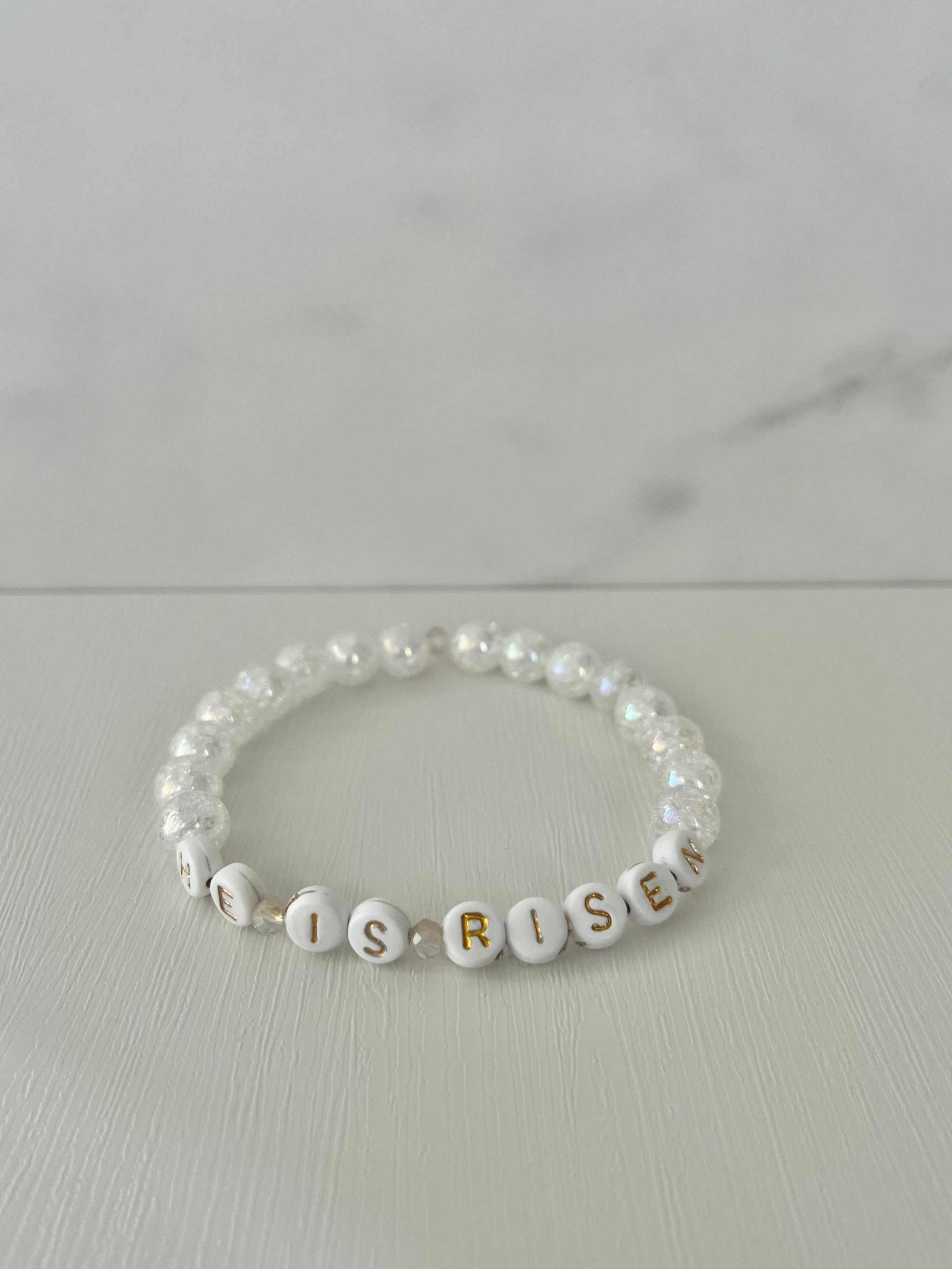 Pearl bracelet with letter beads spelling 'IS RISES' on a light background