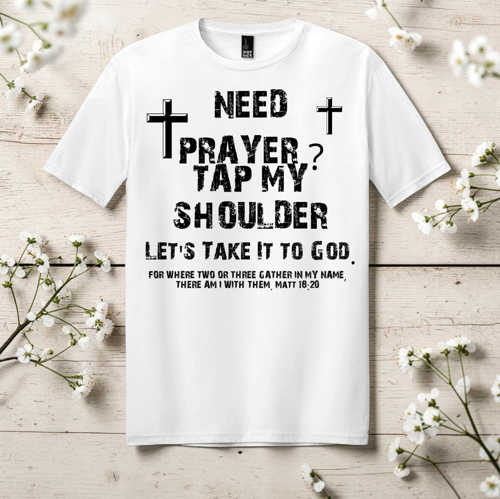 White t-shirt with black text and crosses on a wooden surface with white flowers.