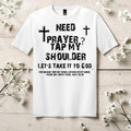 White t-shirt with black text and crosses on a wooden surface with white flowers.